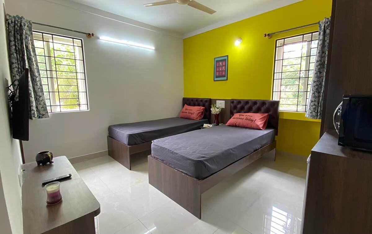 Twin sharing furnished room at Krushna Boys PG Navrangpura with TV, study desk, and yellow accent wall